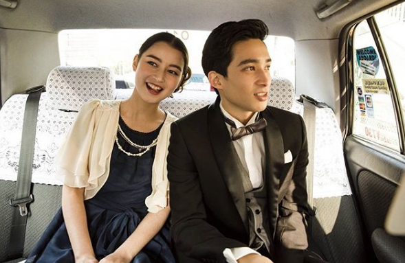 女性　結婚式用のネイビーのワンピースドレスにベージュのボレロ。メンズ黒のタキシードに白のウイングカラーシャツ、ライトグレーのベストにモノトーンのボウタイ